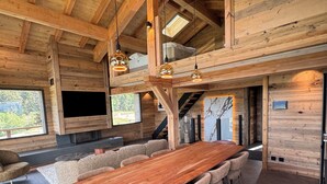 A spacious wooden interior with a long dining table, comfortable seating, and a fireplace. - Luxury 115-square-meter chalet in a ski resort, ideal for two families (8–10 people) (Saint-Pierre-dels-Forcats)