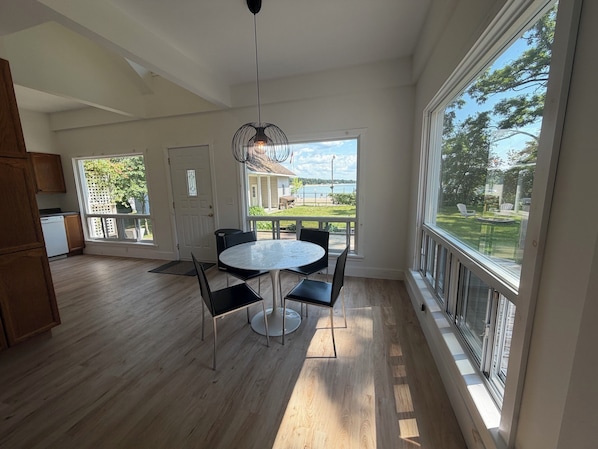 A modern kitchen with wooden cabinets, a dining area with a round table and chairs, and large windows offering a view of the outdoors.