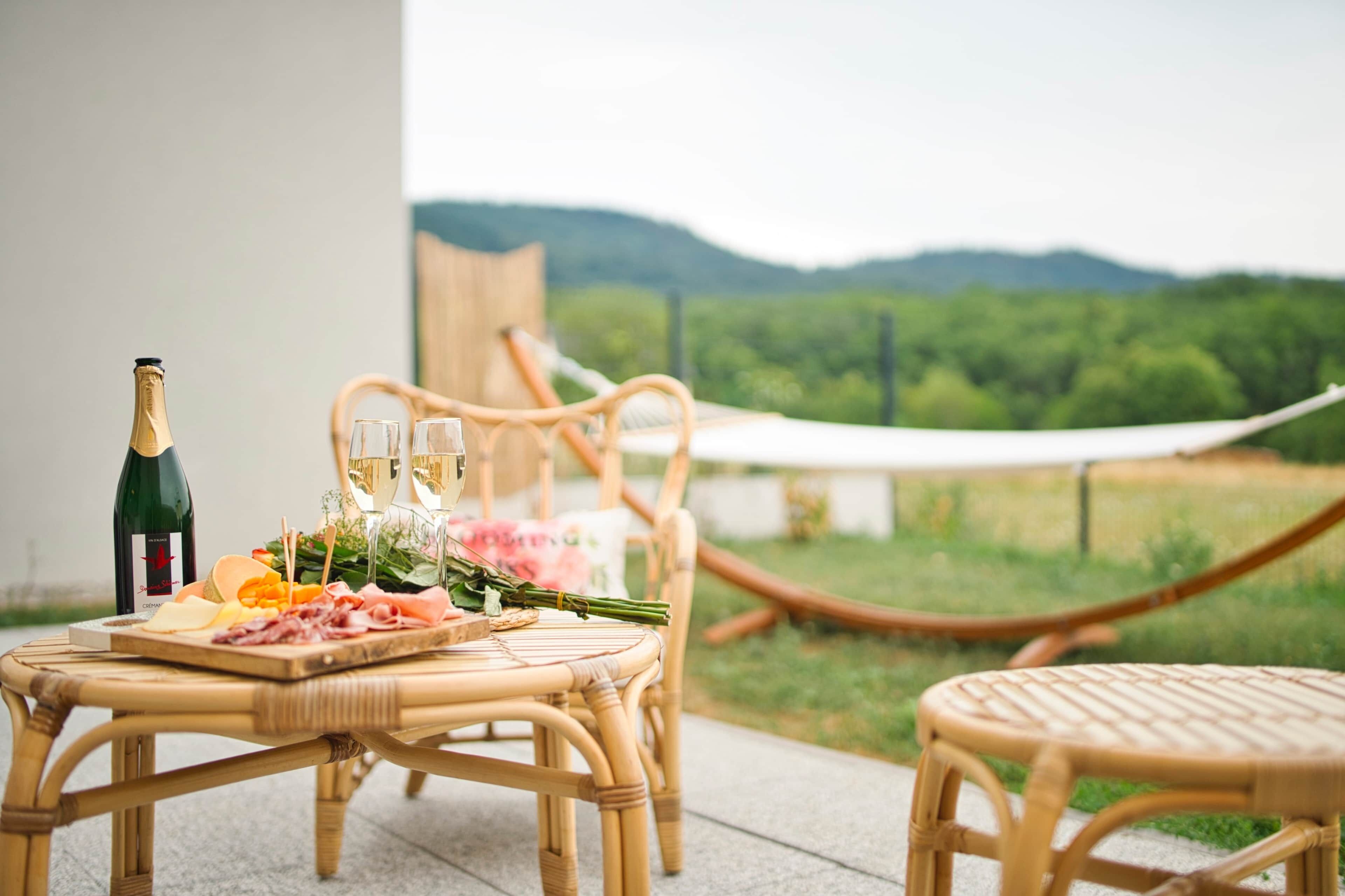 Une table en osier, avec une bouteille de champagne, des verres et une planche de charcuterie.