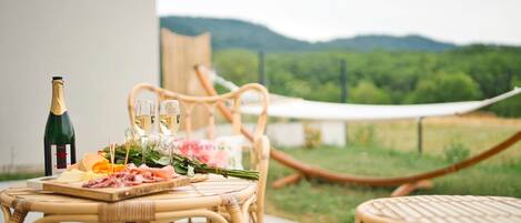 A wicker table with a bottle of champagne, glasses, and a charcuterie board.