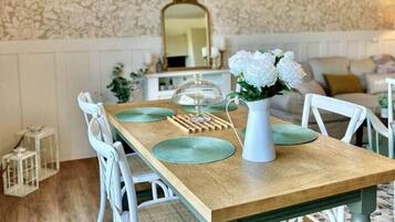 Un comedor con mesa de madera, sillas blancas, lámpara colgante y papel tapiz con estampado floral.