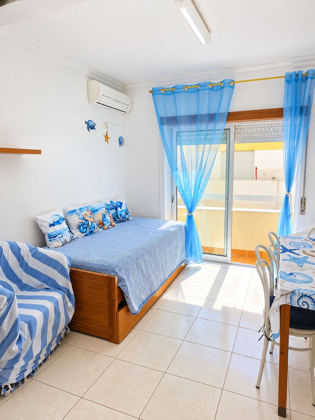 Une chambre à coucher avec un lit, une table et une chaise. Il y a une fenêtre avec des rideaux bleus.