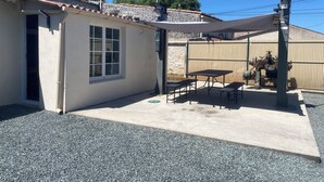 A patio with a table and benches, a small window, and a fenced area with a metal structure. - Air-conditioned house in an ideal location (Montpellier-de-Médillan)