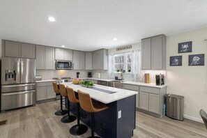 A modern kitchen with grey cabinets, stainless steel appliances, and a central island with bar stools. - Private heated Pool ~ Themed Pub ~ Hot Tub ~ Theater ~Holmes Hideaway (Long Pond)