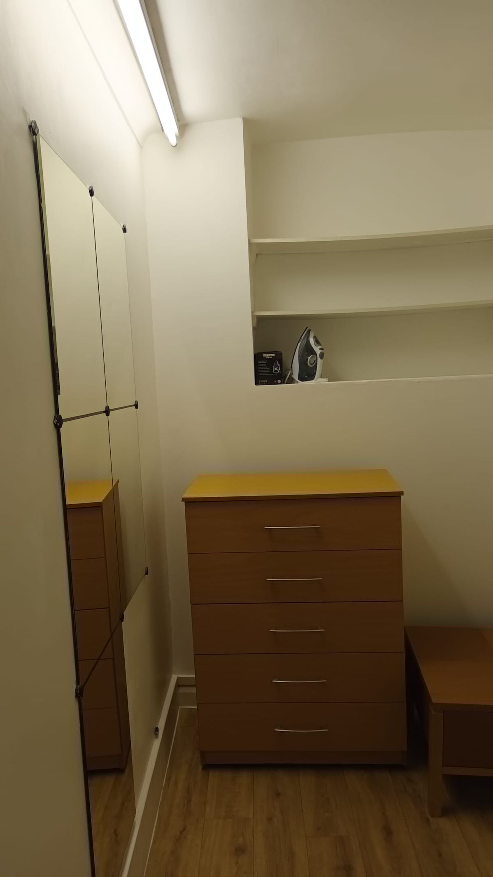 Een kamer met een houten dressoir, een spiegel en een plankje met een radio.