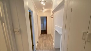 Un estrecho pasillo con suelo de madera y paredes blancas que conduce a una habitación con una lámpara en el techo.