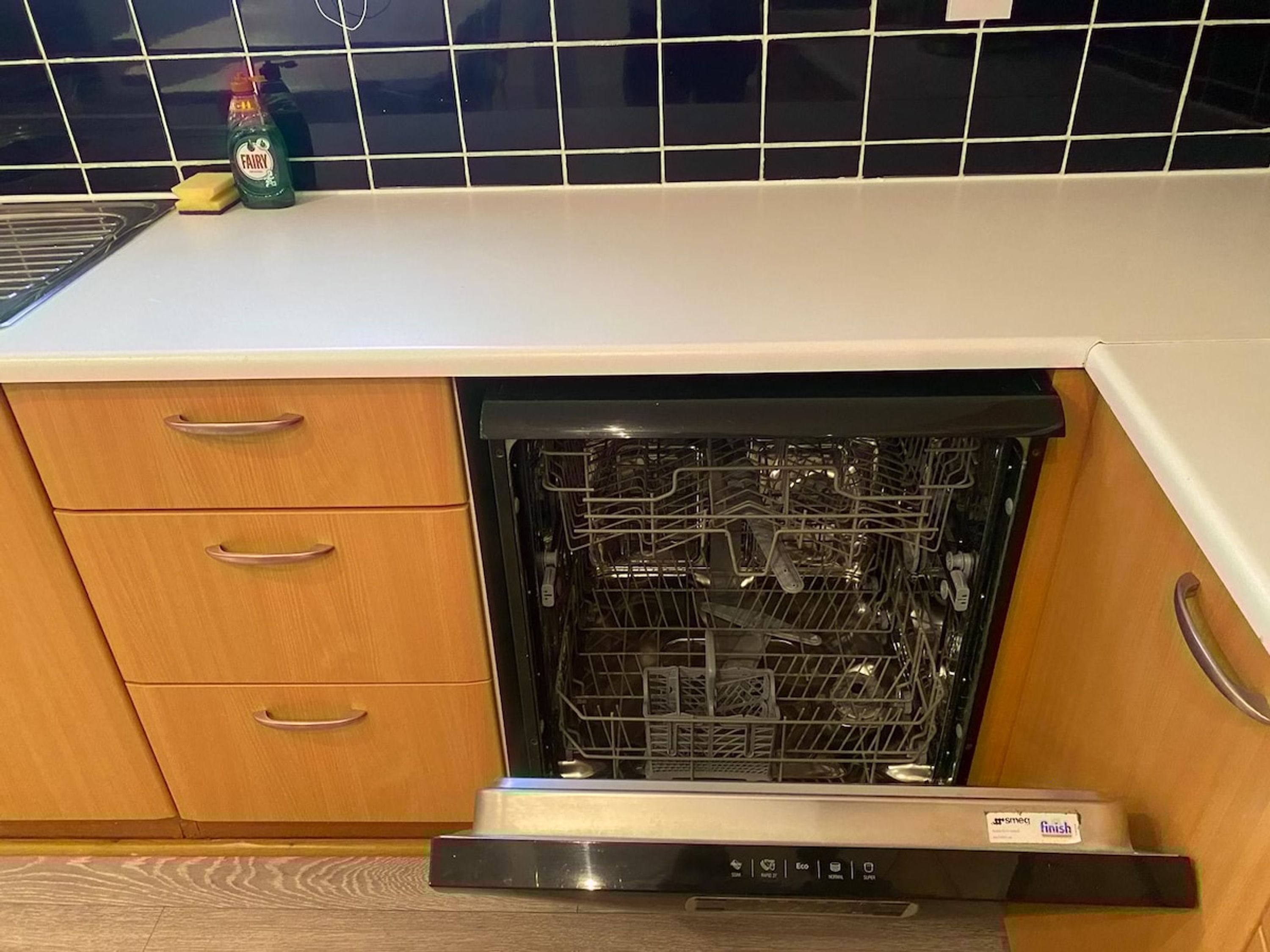 A kitchen with a dishwasher, wooden cabinets, and a tiled backsplash.