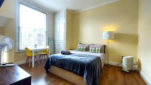 Une chambre à coucher comprenant un lit, un bureau, des chaises, une lampe sur pied et un radiateur.