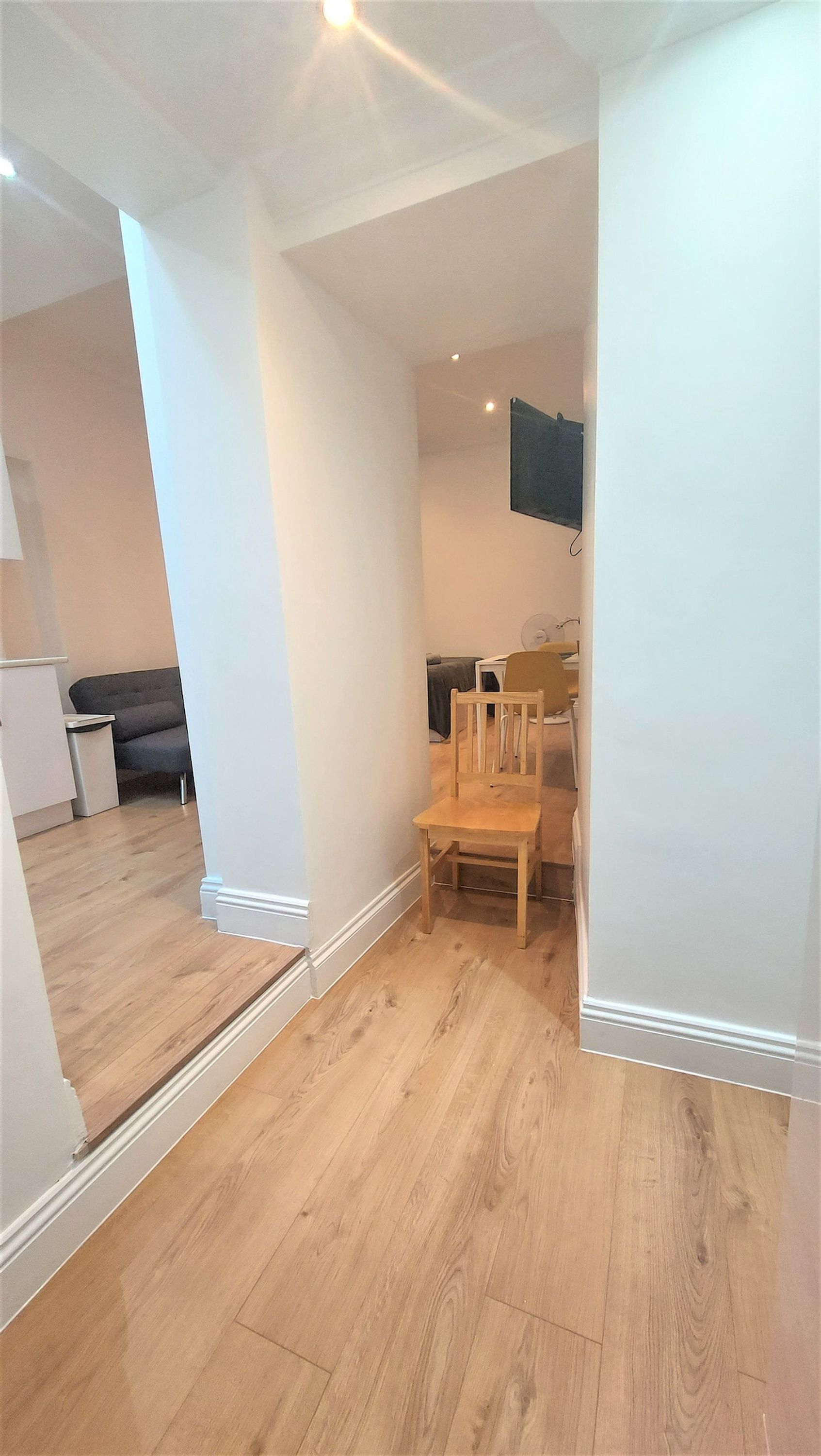Une pièce avec un plancher en bois, une chaise en bois, un téléviseur fixé au mur et un canapé à l’arrière-plan.