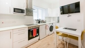 Ett modernt kök med vita skåp, mikrovågsugn, ugn och tvättmaskin.