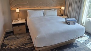 Une chambre d’hôtel avec un grand lit, deux lampes de chevet, un téléphone, une table de chevet et une fenêtre avec des rideaux.