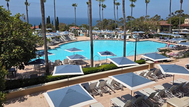 Un complexe hôtelier doté d’une piscine, de chaises longues, de parasols et de palmiers.