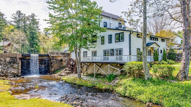 Uma casa com uma cachoeira, uma ponte de pedra e um jardim bem cuidado.