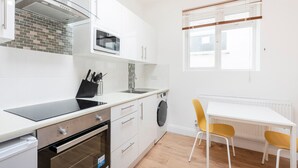 Une cuisine compacte équipée d’un four à micro-ondes, d’un four et d’un évier, un coin repas avec une table et des chaises, et une fenêtre avec des stores.