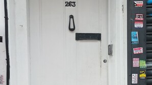 Une porte blanche portant le numéro 263, une fente noire pour le courrier et une poignée en métal.