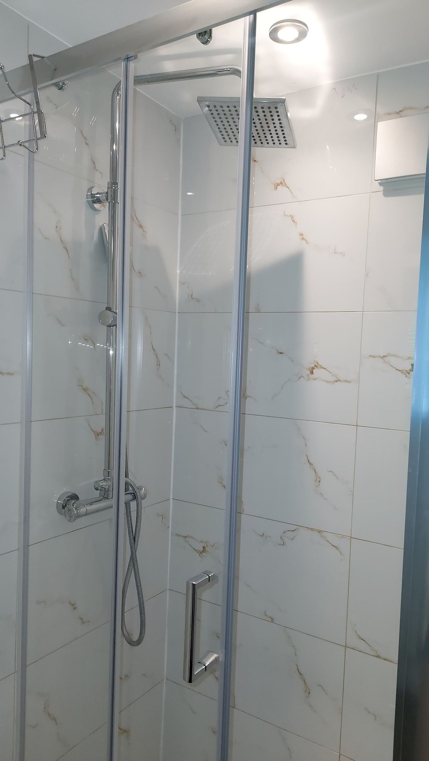Um chuveiro com paredes de vidro, um chuveiro manual, uma torneira fixada na parede e um painel de controle.