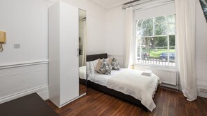 A bedroom with a bed, a window with curtains, a radiator, and a door leading to another room. - Lovely Studio with park view in Camden/Kings Cross (London)