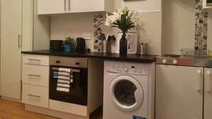 Eine kompakte Küche mit weißen Schränken, einem Backofen, einer Waschmaschine und einer Mikrowelle.