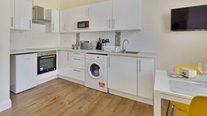 Eine kompakte Küche mit weißen Schränken, einer Mikrowelle, einer Waschmaschine, einem kleinen Backofen und einem Essbereich mit Tisch und Stühlen.