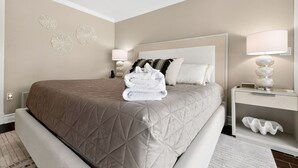 A hotel room with a large bed, a bedside table with a lamp, decorative wall art, and a folded towel on the bed. - Waterfront Home with Pool & Dock (Siesta Key)