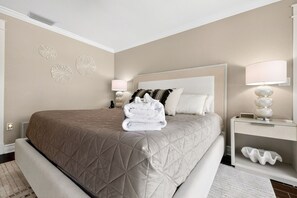 A hotel room with a large bed, a bedside table with a lamp, decorative wall art, and a folded towel on the bed. - Waterfront Home with Pool & Dock (Siesta Key)
