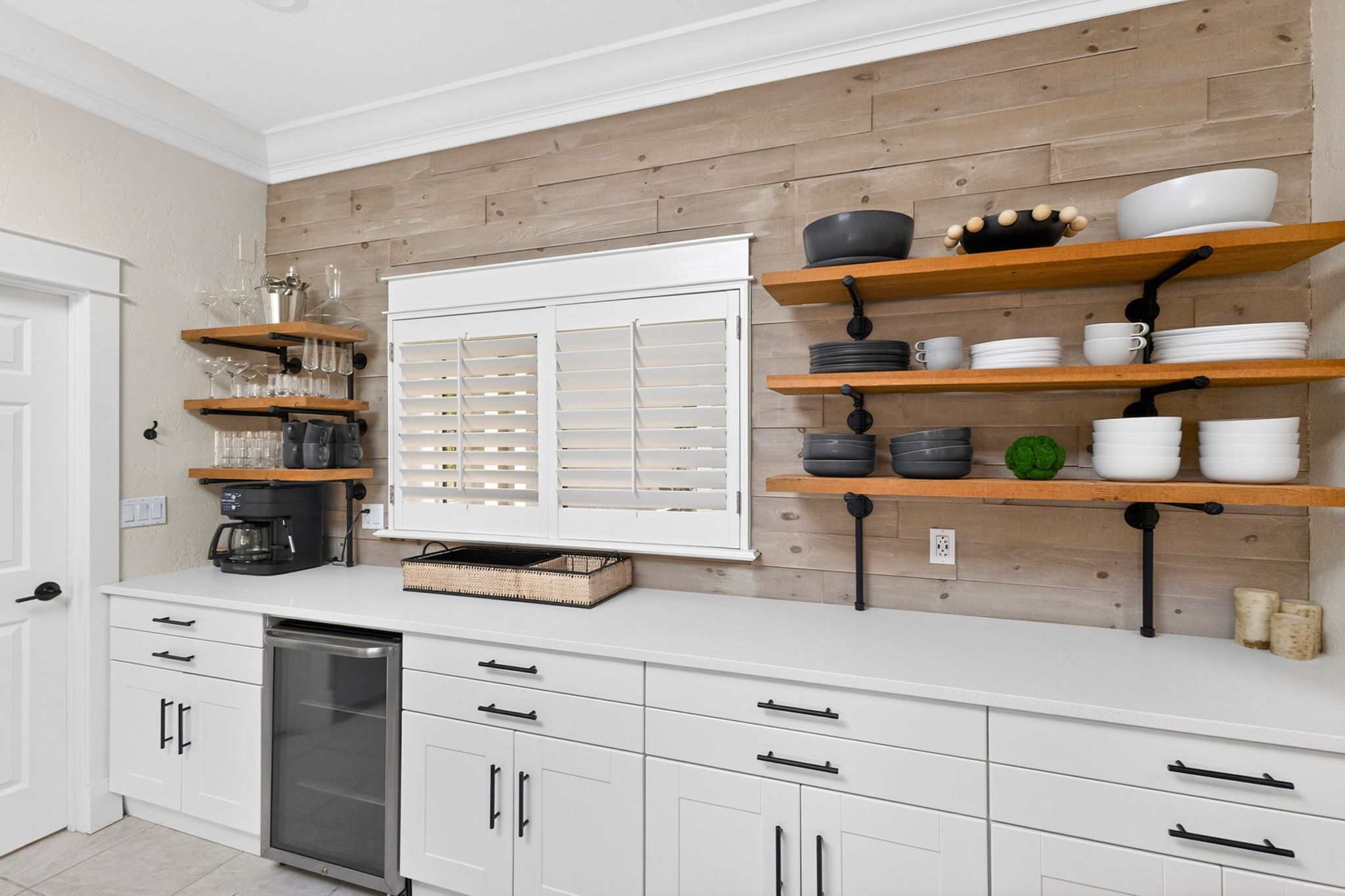 A modern kitchen with white cabinetry, wooden shelves, and a variety of kitchenware.