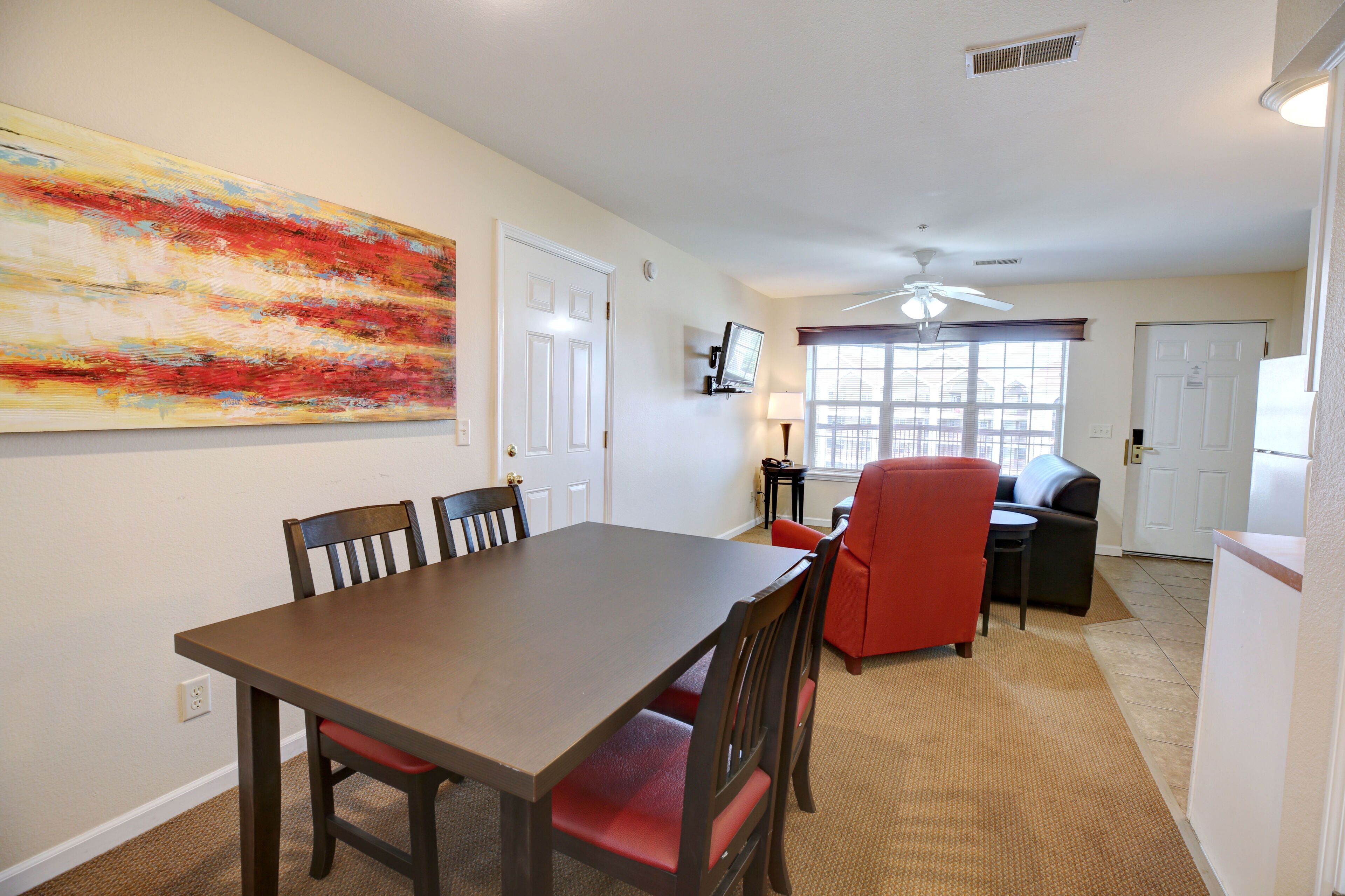 A dining area with a wooden table and chairs, a red sofa, and a large abstract painting on the wall.