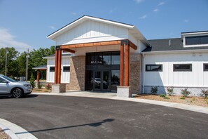 A building with a covered entrance, a parking lot, and a car parked in front. - 1BR Condo w/ Private Balcony & Full Kitchen (Branson)