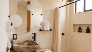 Un baño moderno con tocador de madera, inodoro blanco, zona de ducha y espejo con detalles decorativos.