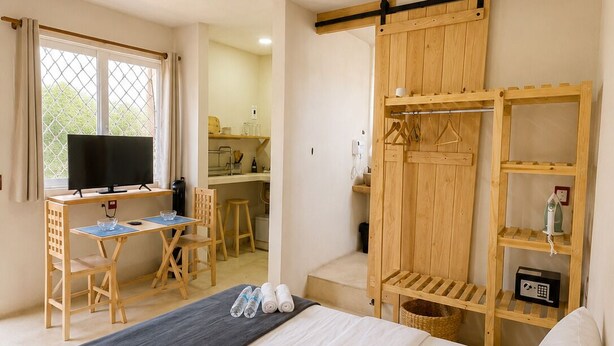 Un dormitorio con cama, escritorio con televisor, armario de madera y ventana con cortinas.