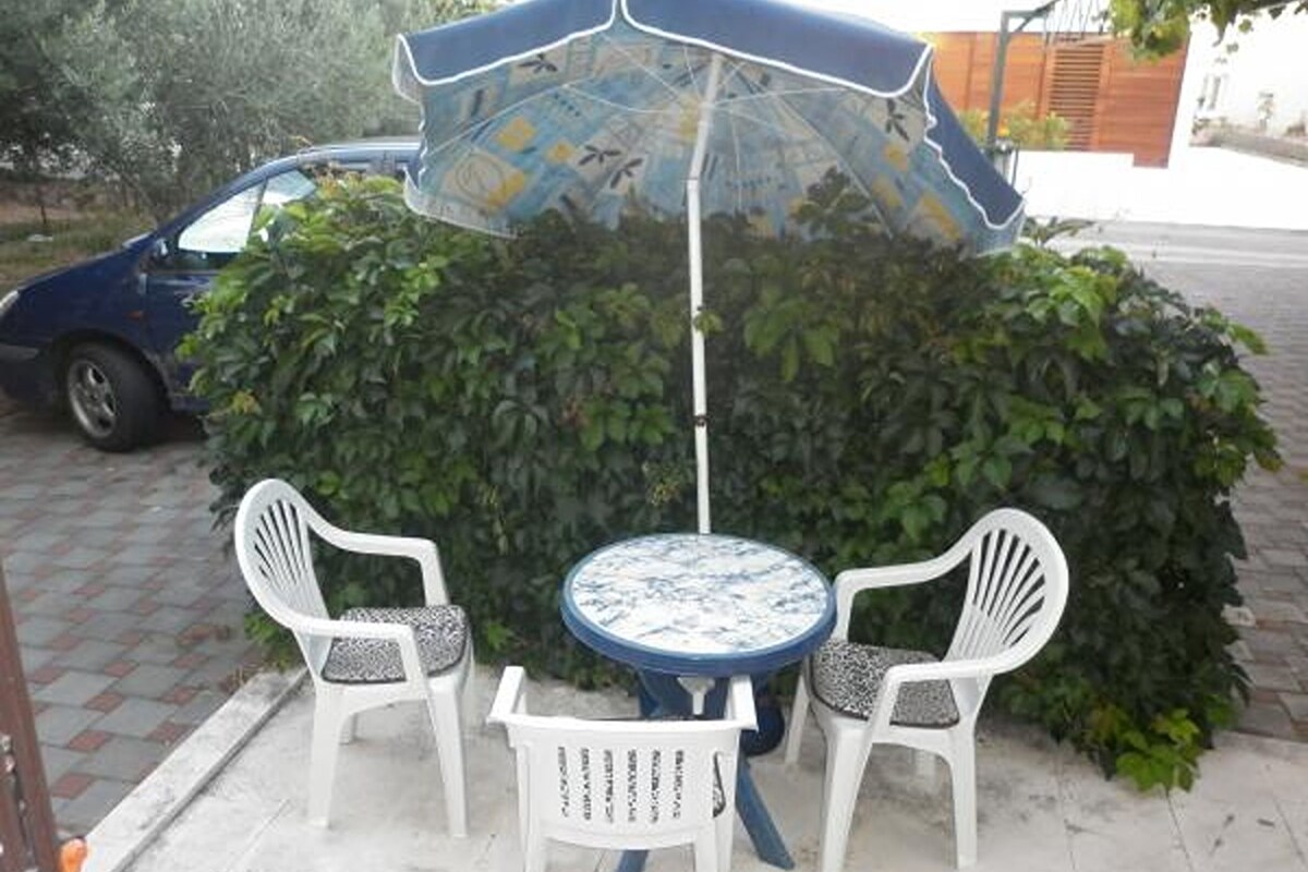 A small outdoor seating area with a table and two chairs, an umbrella, and a hedge in the background.
