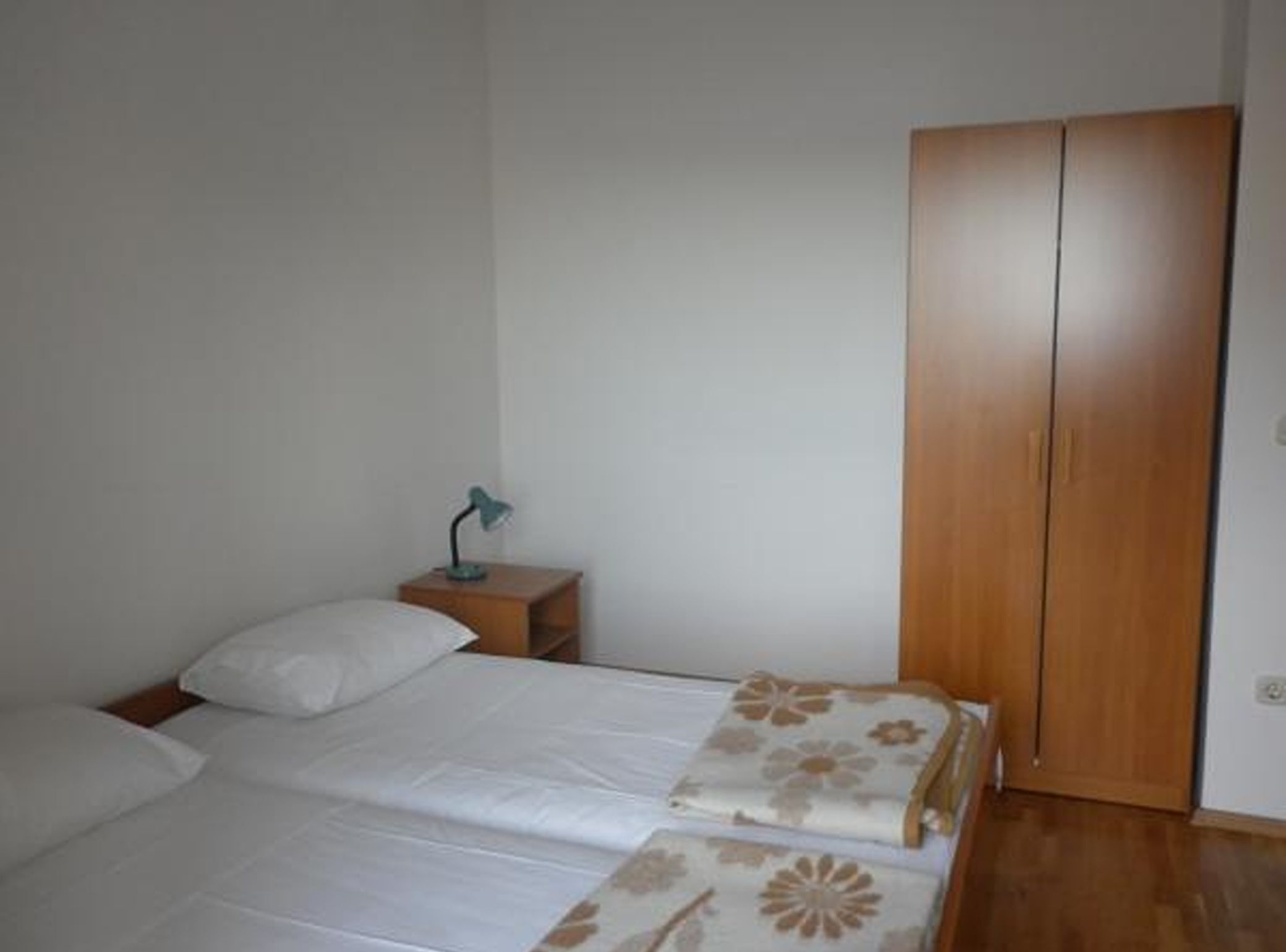 A bedroom with a bed, a nightstand, a lamp, and a wardrobe.