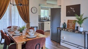 Un'area pranzo con un tavolo di legno apparecchiato per quattro persone, una cucina sullo sfondo e un cartello di benvenuto appeso al muro.