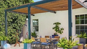 Ein Poolbereich mit überdachter Terrasse, Sitzgelegenheiten und Kübelpflanzen.
