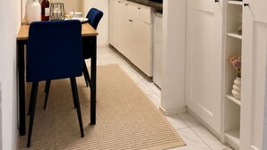 Una cocina compacta con armarios blancos, un comedor con una silla azul y una alfombra pequeña.