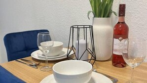 Una mesa de comedor decorada con platos, cuencos y cubiertos blancos, un jarrón con tulipanes, una botella de vino tinto y un candelabro de metal negro.