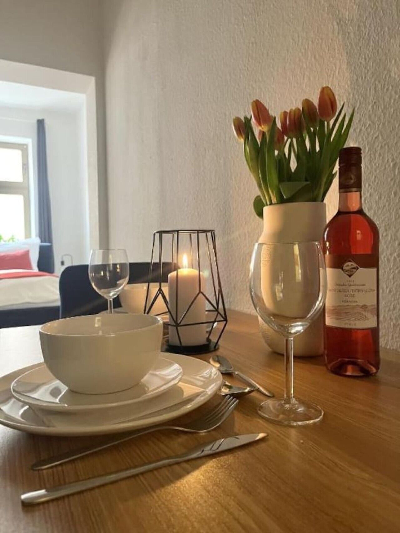 Ein Esstisch mit Kerze, Tulpenvase, Weinflasche und Besteck.