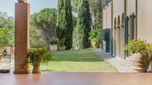 Une terrasse couverte agrémentée d’une pergola en bois, d’un pilier en briques et de plantes en pot.