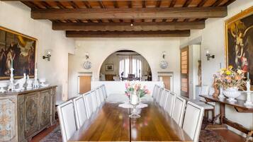 Una sala da pranzo con un lungo tavolo di legno, sedie bianche, un vaso di fiori e un quadro appeso al muro.