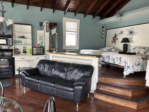 Ein gemütliches Zimmer mit einer schwarzen Ledersofa, einem Bett mit floralem Bettwäsche, einer Holztreppe und einer Küchenzeile inklusive Mikrowelle.
