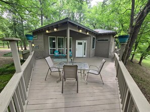 Eine Holzterrasse mit überdachter Veranda, Sitzgelegenheiten im Freien und einem kleinen Gebäude mit Tür und Fenstern.