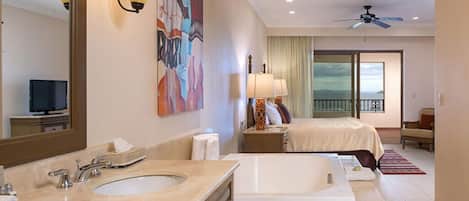 Habitación de hotel con una cama grande, baño separado con bañera, balcón con vistas y ventilador de techo.