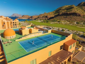 Un court de tennis situé sur un toit, offrant une vue sur la mer et les montagnes.