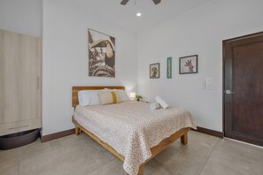 A bedroom with a wooden bed, a large wall art of a toucan, and a door on the right. - CU11 Private 4BR Oasis-Pool-Guest House-Close to Beach (tamarindo)