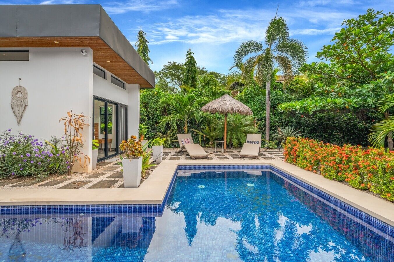 Un área de piscina moderna con una piscina azul cristalina, sillas de descanso y plantas tropicales.