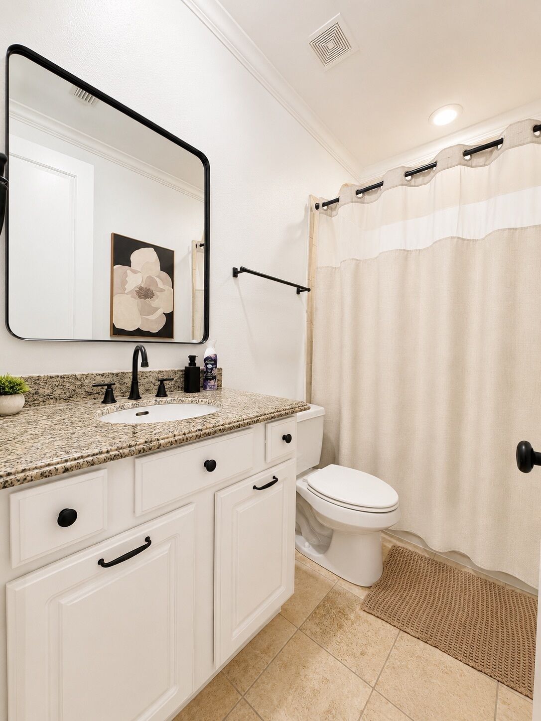 Un baño con un lavabo blanco, grifo negro y un espejo encima. Se ve un inodoro y una cortina de ducha.