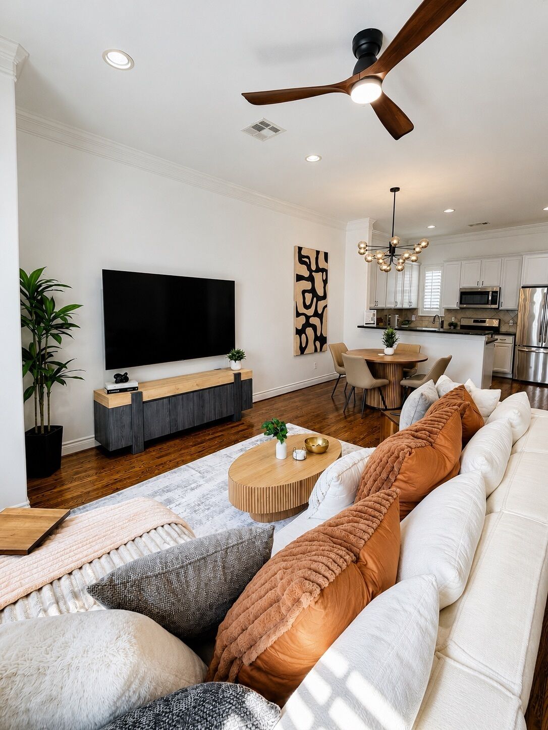 Ein modernes Wohnzimmer mit Flachbildfernseher, Deckenventilator, Essbereich und Küche mit Edelstahlgeräten.