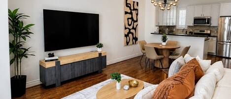Ein modernes Wohnzimmer mit Flachbildfernseher, Deckenventilator, Essbereich und Küche mit Edelstahlgeräten.