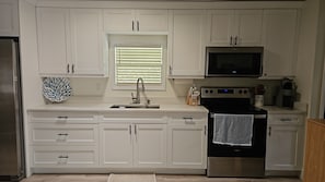 Eine moderne Küche mit weißen Schränken, einem Edelstahl-Kühlschrank, einer Mikrowelle und einem Backofen.