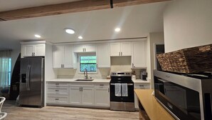 A modern kitchen with white cabinetry, a stainless steel refrigerator, a stove, and a large window. - Boaters dream! Waterfront home in Bonita Springs - Estero Bay in minutes (Bonita Springs)